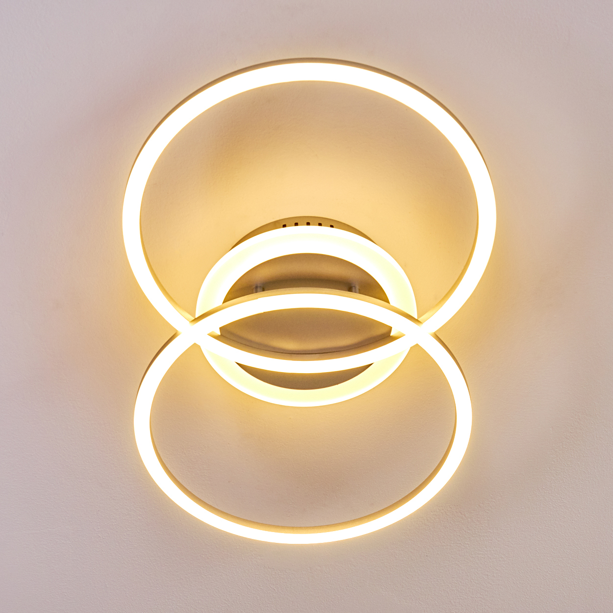 Moderne Deckenleuchte. Sie hat drei überlappende Ringe, die mit warmweißem Licht vor einer weißen Decke leuchten.