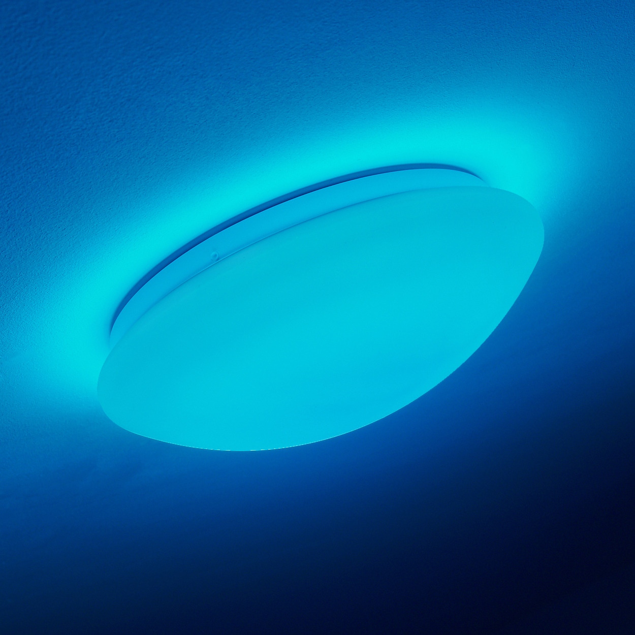Eine moderne, runde Deckenlampe, die blaues Licht ausstrahlt. Sie ist an einer strukturierten weißen Decke montiert.