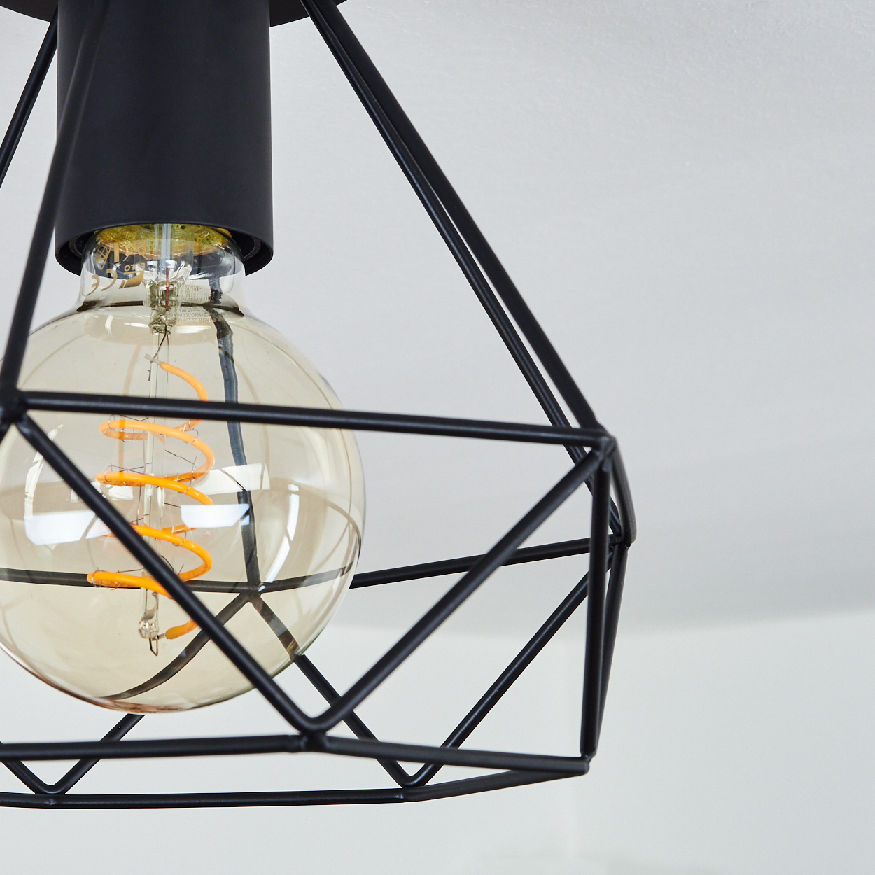 Eine schwarze geometrische Pendelleuchte mit einer großen, leuchtenden Glühbirne. Der Hintergrund ist eine schlichte weiße Decke.