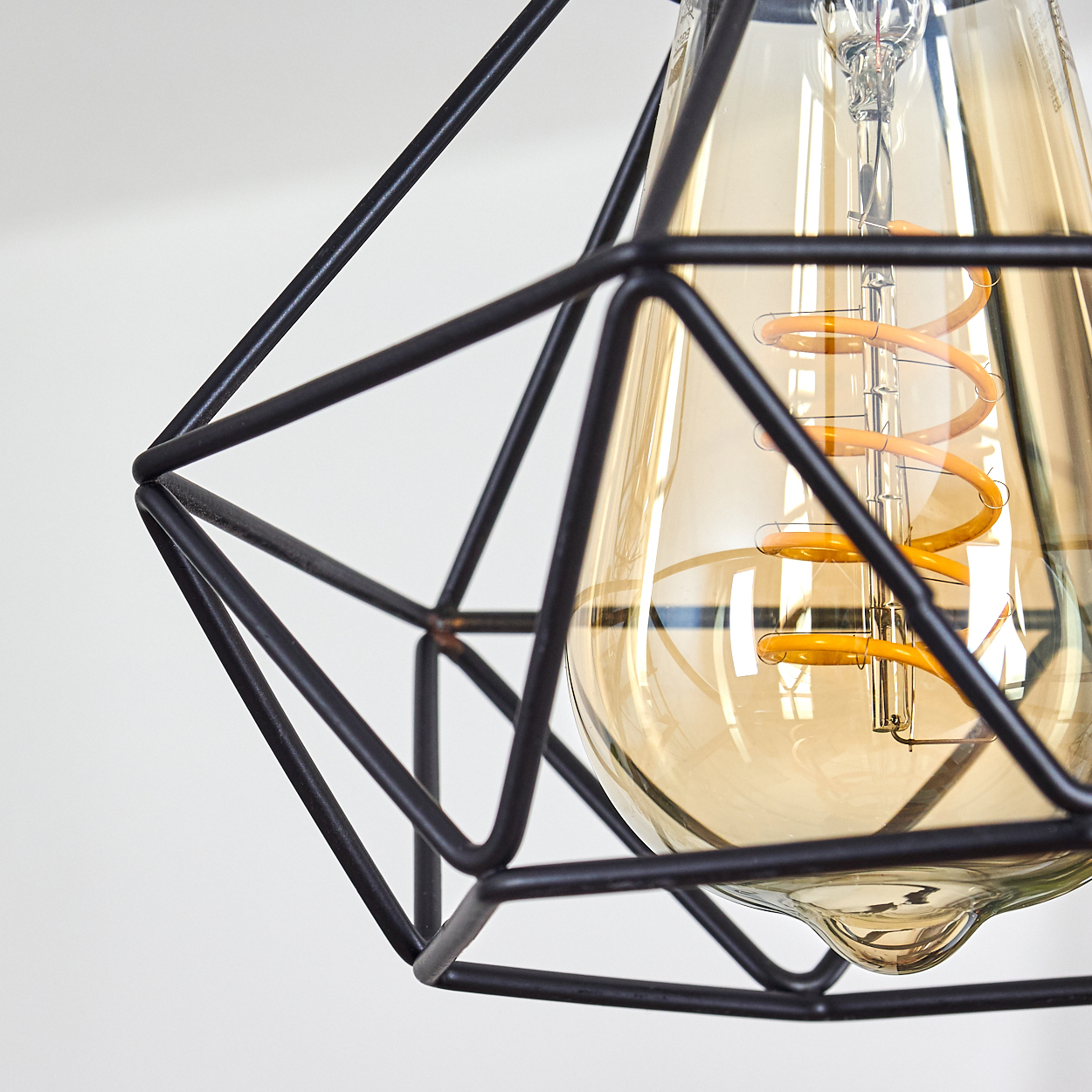 Nahaufnahme eines schwarzen, geometrischen Lampenschirms mit einer warm getönten Glühbirne. Der Hintergrund ist schlicht weiß.