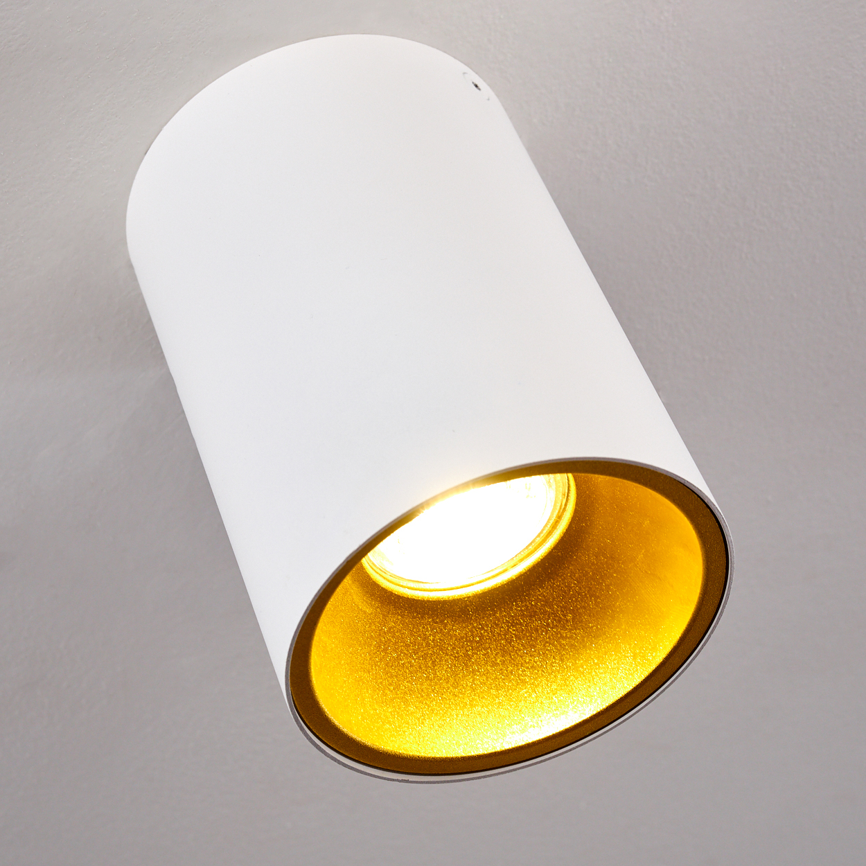 Ein weißer, zylindrischer Scheinwerfer mit goldenem Innenraum, vor hellgrauem Hintergrund. Das Licht scheint hell.