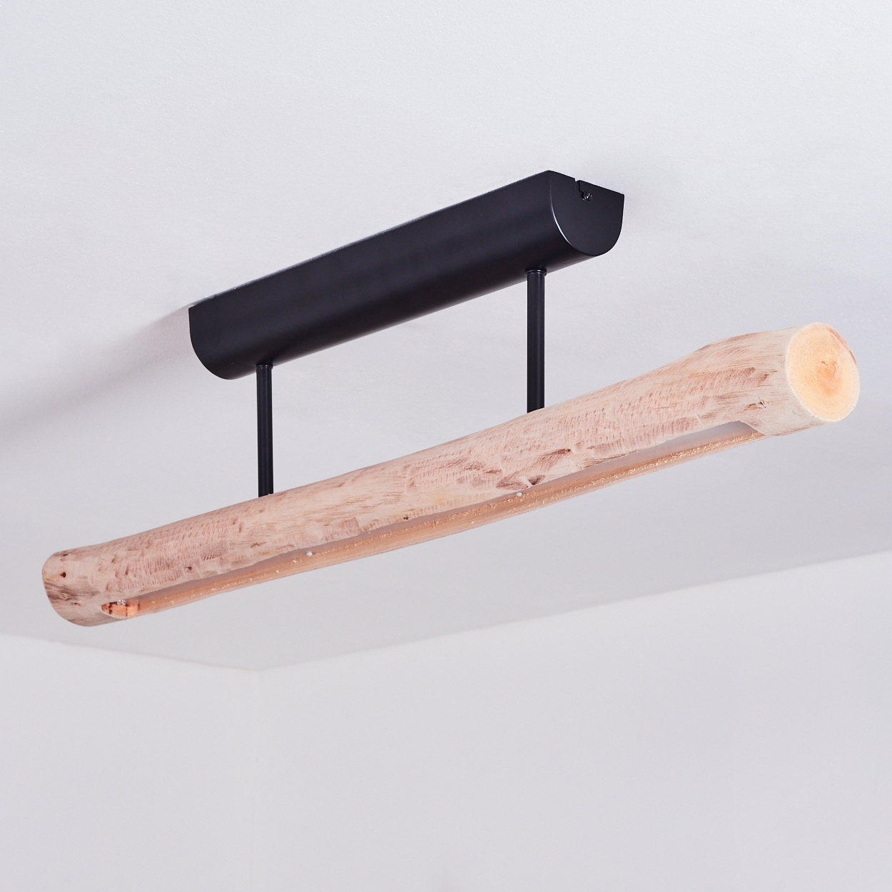 Eine holzförmige Lampe hängt von der Decke. Sie hat einen schwarzen Metallaufsatz. Der Stamm ist hellbraun und rau.