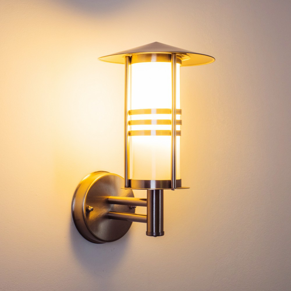 Eine Wandlampe mit zylindrischem Glasschirm und Metallrahmen, beleuchtet vor hellem Hintergrund.