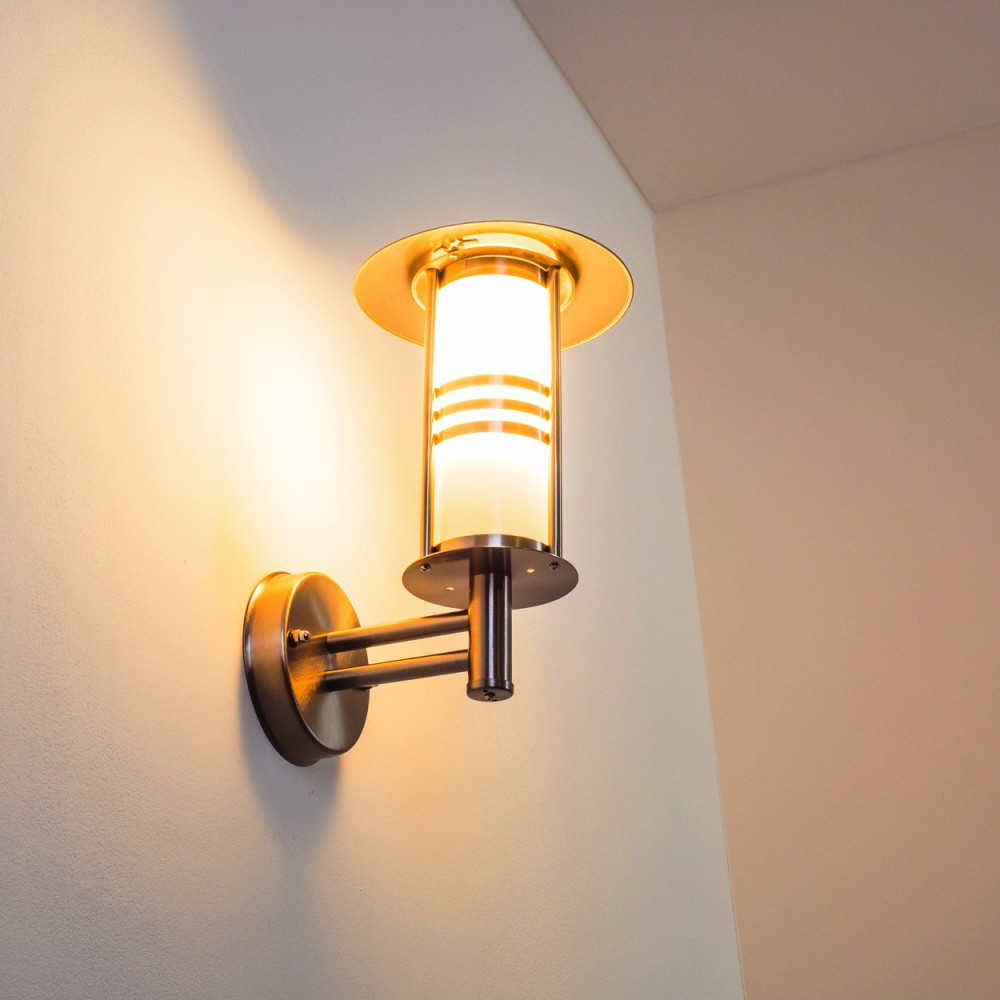 Eine Wandlampe mit zylindrischem, mattiertem Glasschirm leuchtet. Die Lampe hat eine metallische Oberfläche mit rundem Sockel.