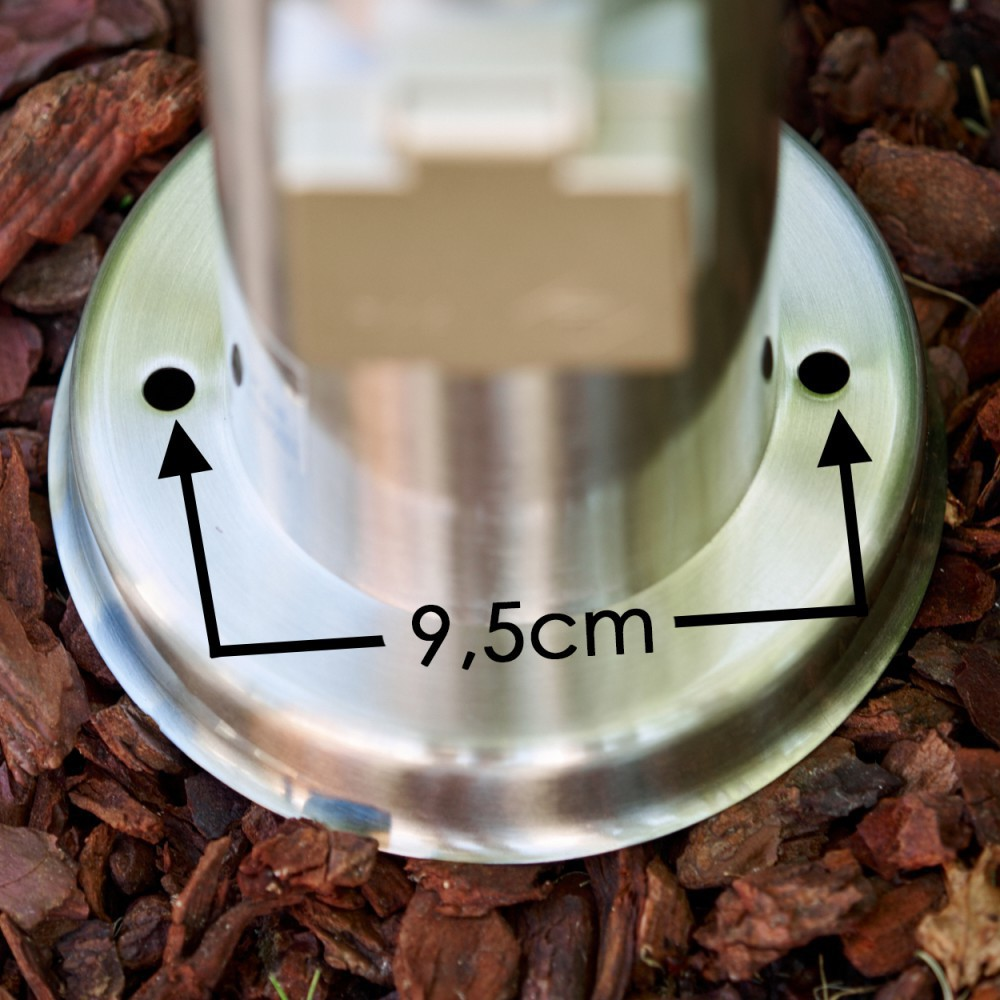 Ein glänzender Metallsockel mit zwei Löchern. Pfeile zeigen auf die Löcher, mit "9,5cm" dazwischen. Der Sockel steht auf braunem Mulch.