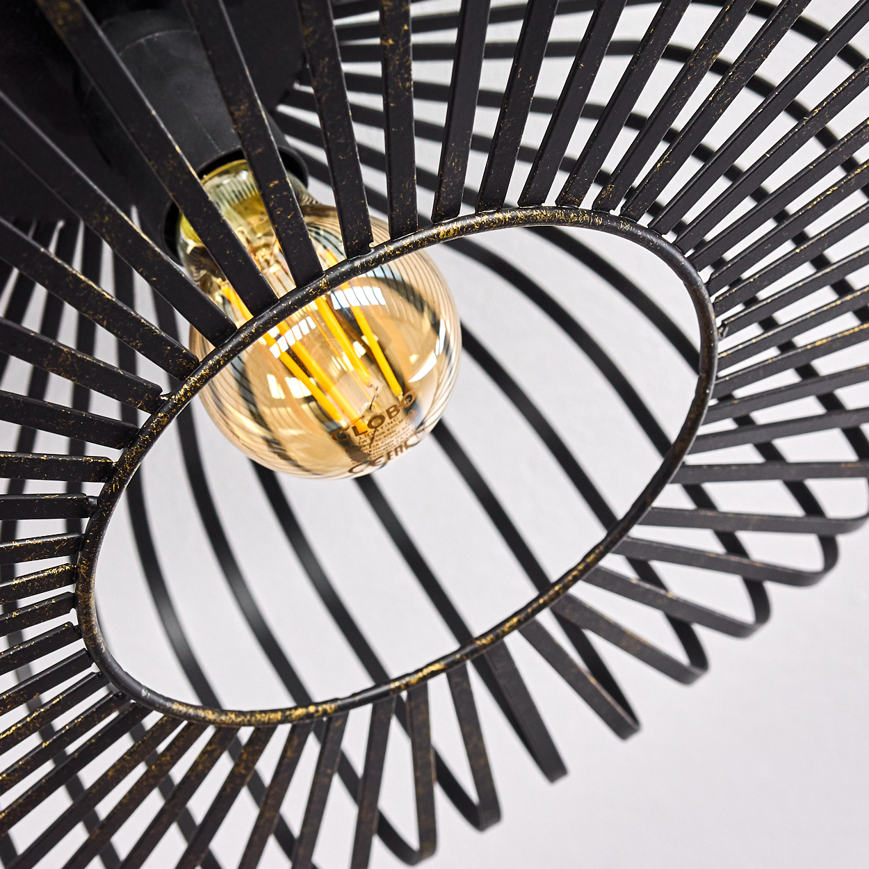 Nahaufnahme einer schwarzen Metalllampe mit einer goldfarbenen Glühbirne. Die Lampe hat ein käfigartiges Design. Weißer Hintergrund.