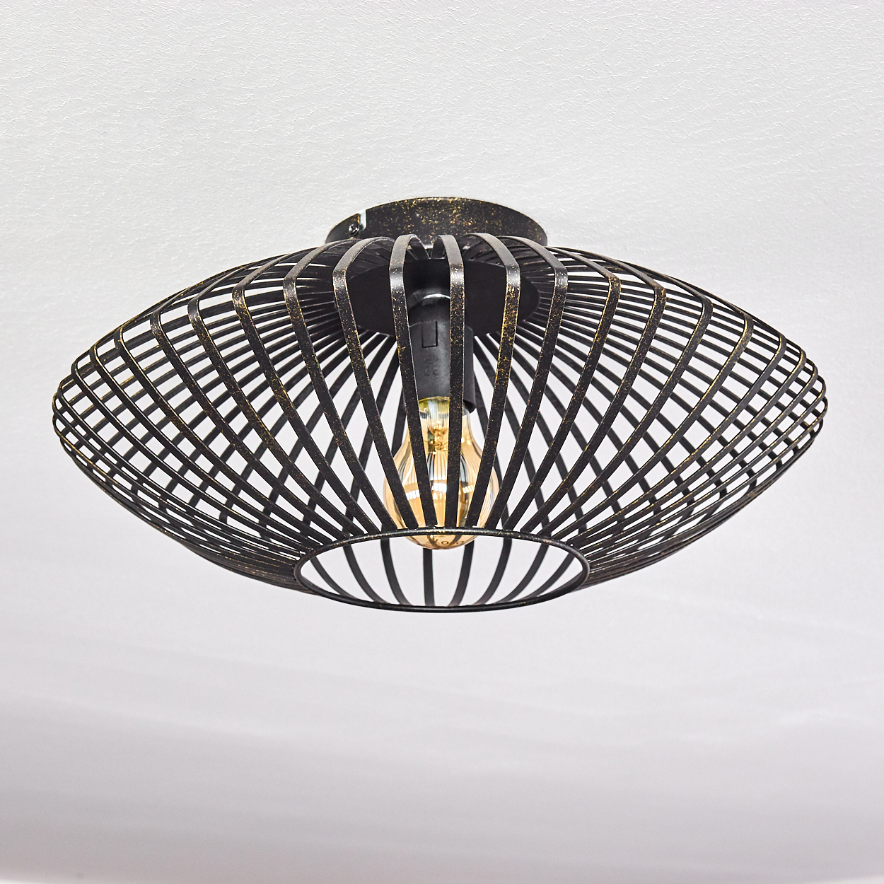 Eine schwarze Metall-Deckenlampe mit Käfigdesign, goldenen Akzenten und einer sichtbaren Glühbirne an einer weißen Decke.