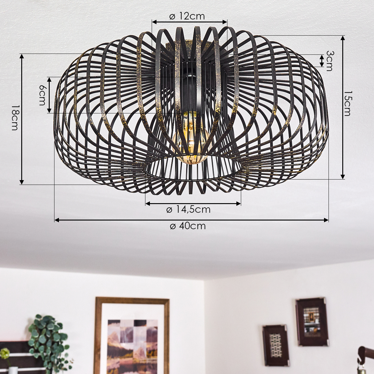 Eine schwarz-goldene Deckenlampe mit Drahtrahmen und beschrifteten Abmessungen. Im Hintergrund eine weiße Decke und gerahmte Bilder.