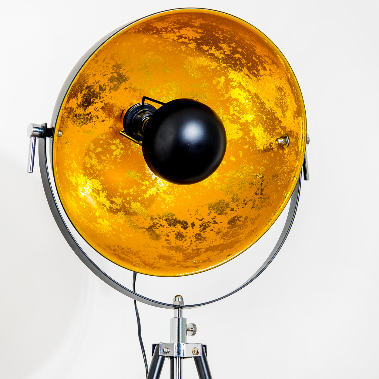 Eine schwarze und goldene Stehlampe. Die Lampe hat einen großen, goldfarbenen Reflektor mit einer schwarzen Glühbirne und einem schwarzen Stativfuß.