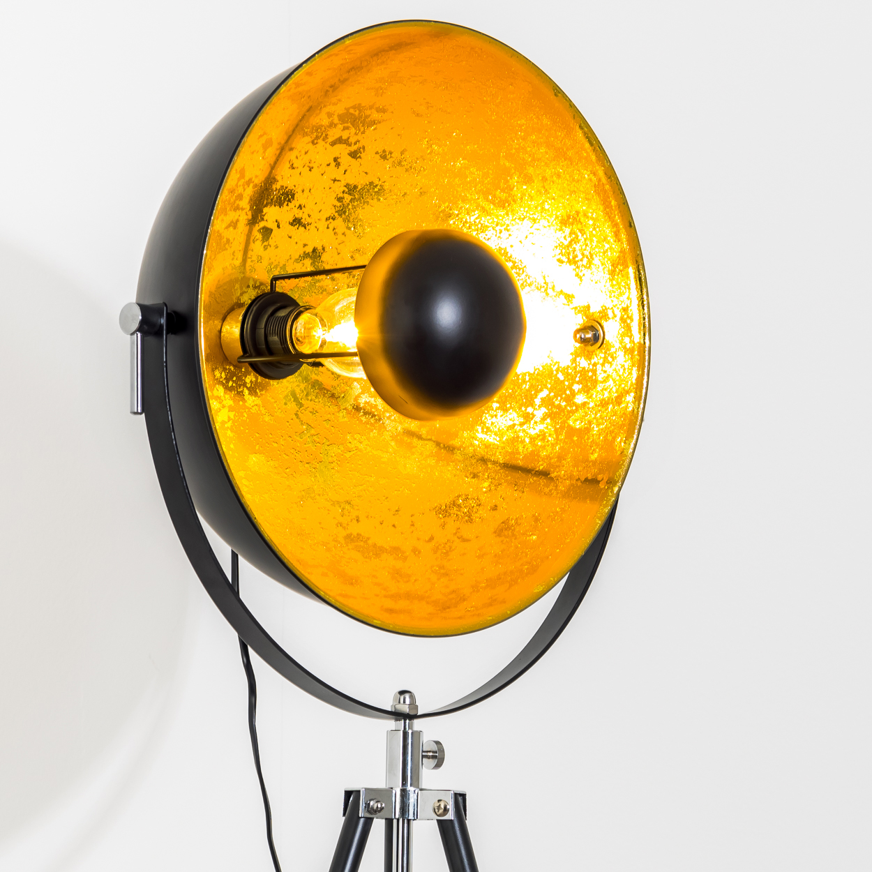 Eine schwarz-goldene Stehlampe mit Stativfuß. Die Lampe hat einen runden Schirm mit goldfarbenem Innenraum und schwarzem Außen.