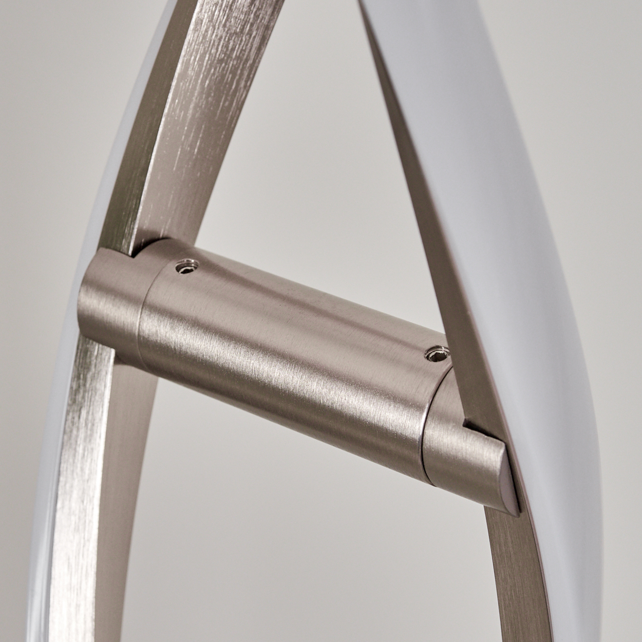Nahaufnahme einer modernen Leuchte. Merkmale gebogene, weiß umrandete Metallarme, die mit einem zylindrischen Metall verbunden sind. Schrauben sichern die Teile.