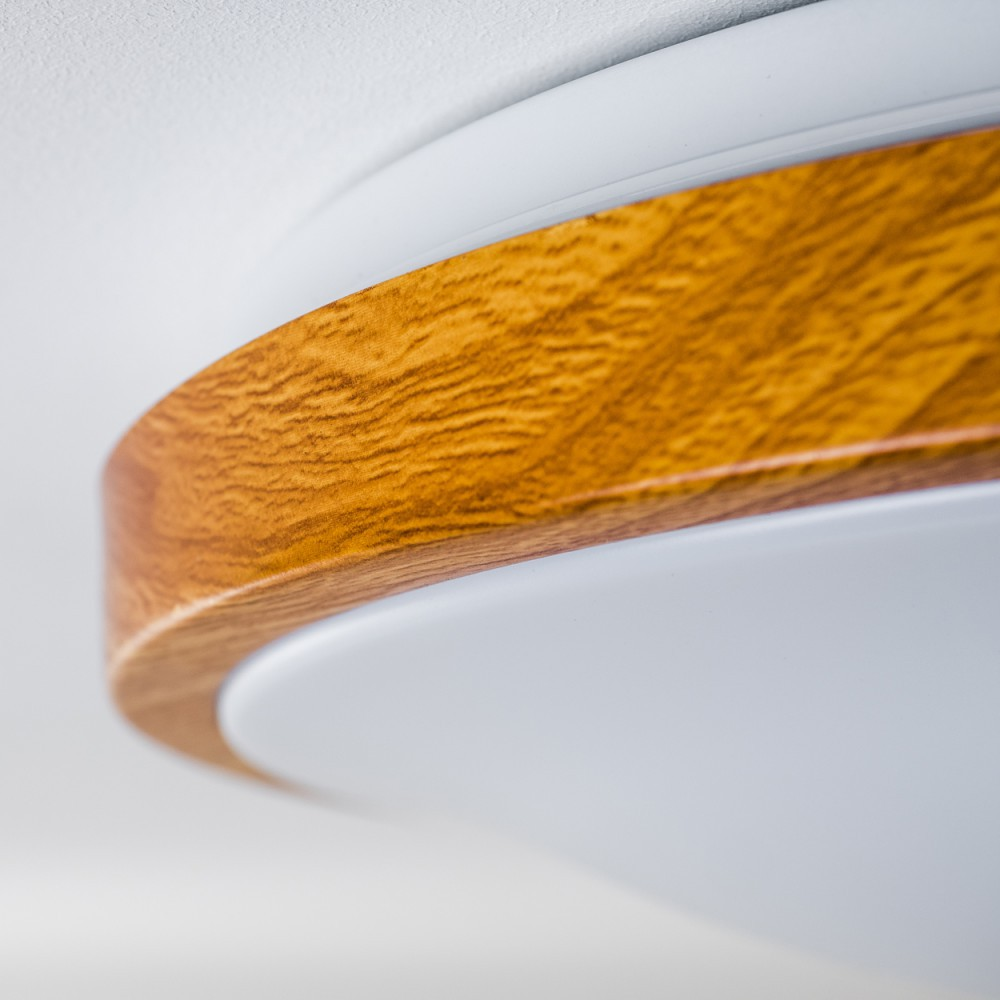 Nahaufnahme einer Deckenleuchte. Die Leuchte hat eine Holzverkleidung auf weißem Hintergrund mit hellem, weichem Licht.
