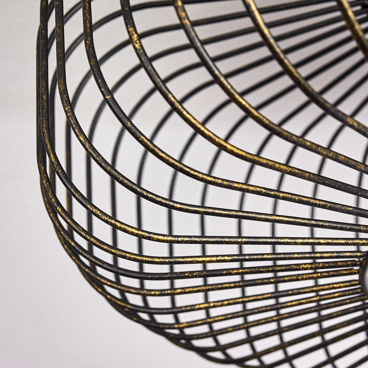 Nahaufnahme eines dekorativen Metallkorbs. Er hat eine schwarz-goldene Farbe und ein gebogenes, offenes Design, vor weißem Hintergrund.