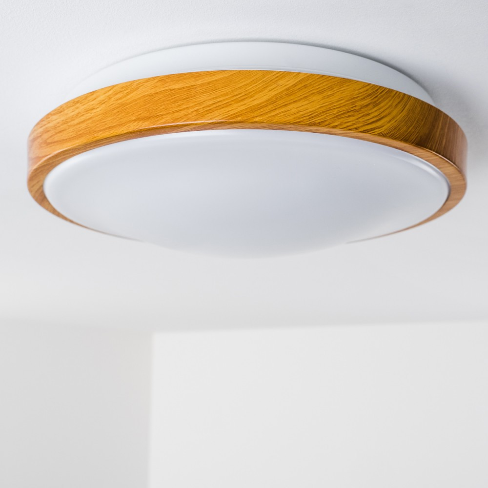 Eine Deckenlampe mit Holzring um einen weißen Diffusor. Der Hintergrund ist schlicht weiß.