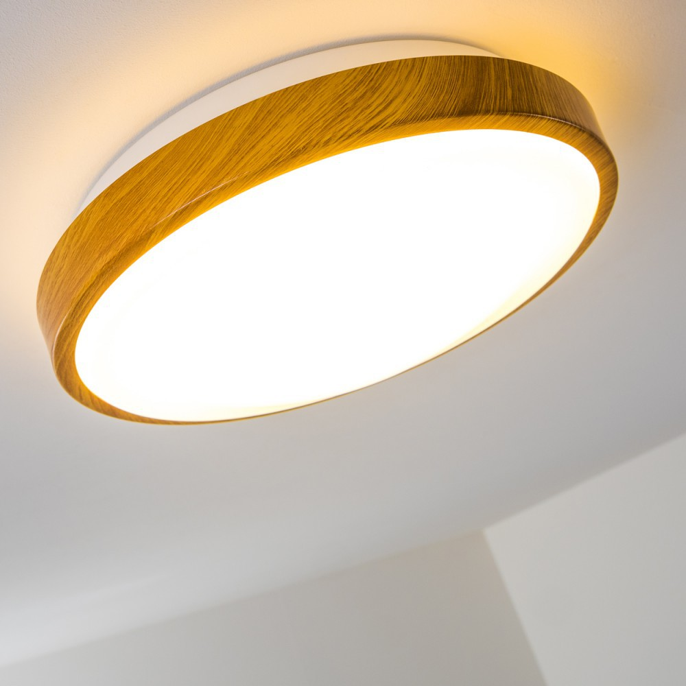 Eine runde Deckenleuchte mit Holzrahmen und hellem weißem Licht. Der Hintergrund ist eine weiße Decke.