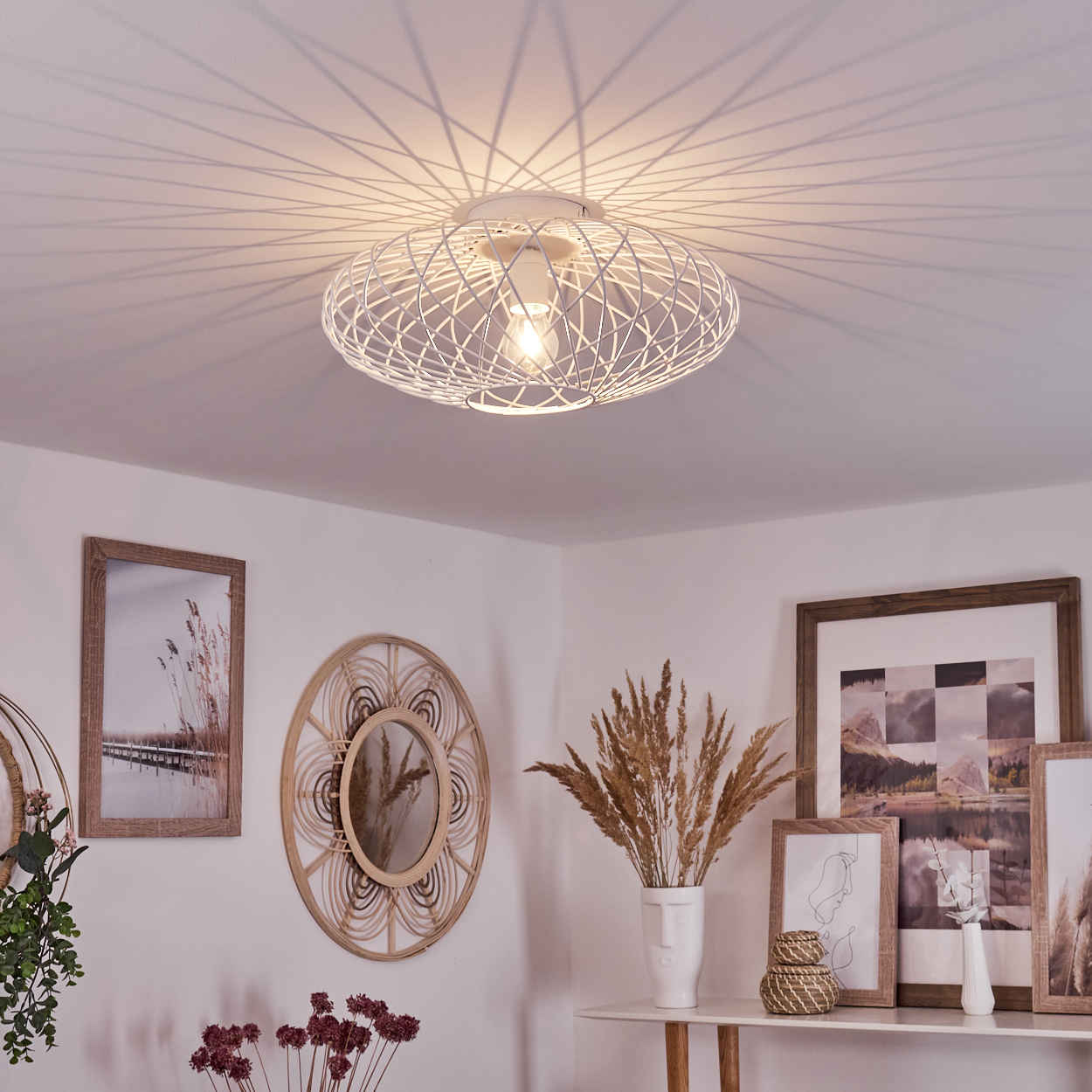 Ein modernes Zimmer mit weißer Deckenlampe, gerahmten Bildern, einem runden Spiegel und einem Tisch mit Dekoration.