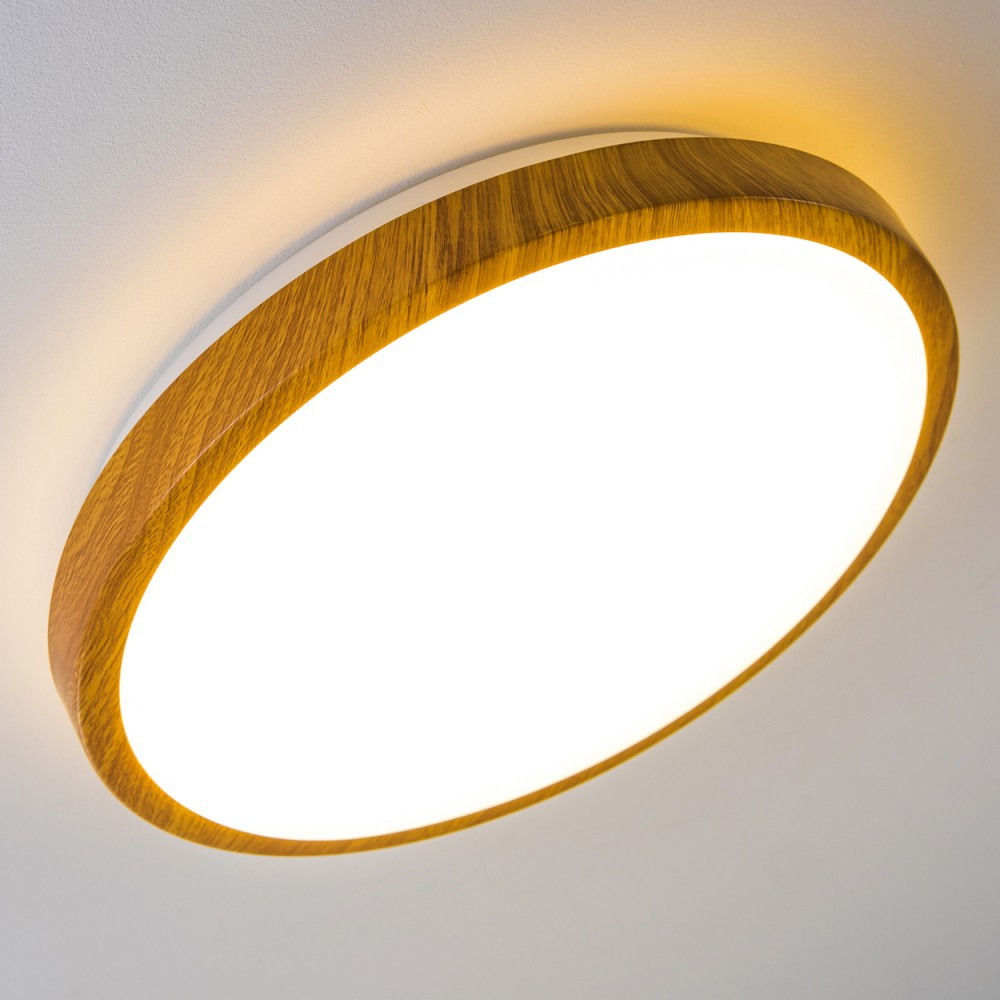 Eine runde Deckenleuchte mit Holzrahmen und heller weißer Lichtquelle. Der Hintergrund ist eine weiße Decke.