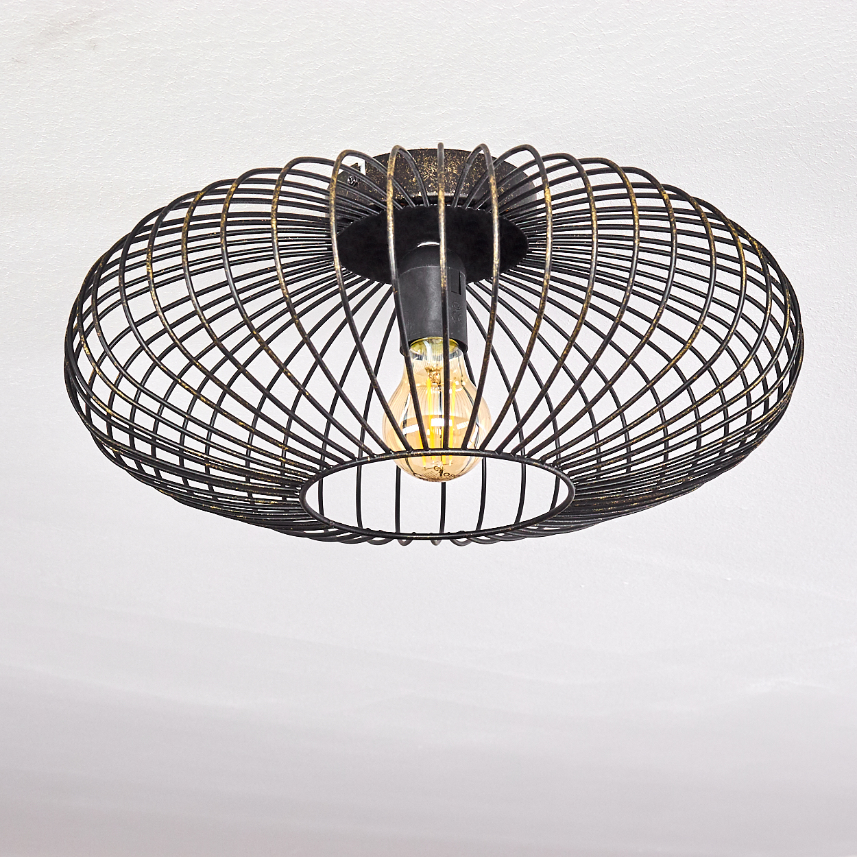 Eine schwarze Deckenleuchte aus Metallkäfig mit einer beleuchteten Glühbirne vor einer weißen Decke.