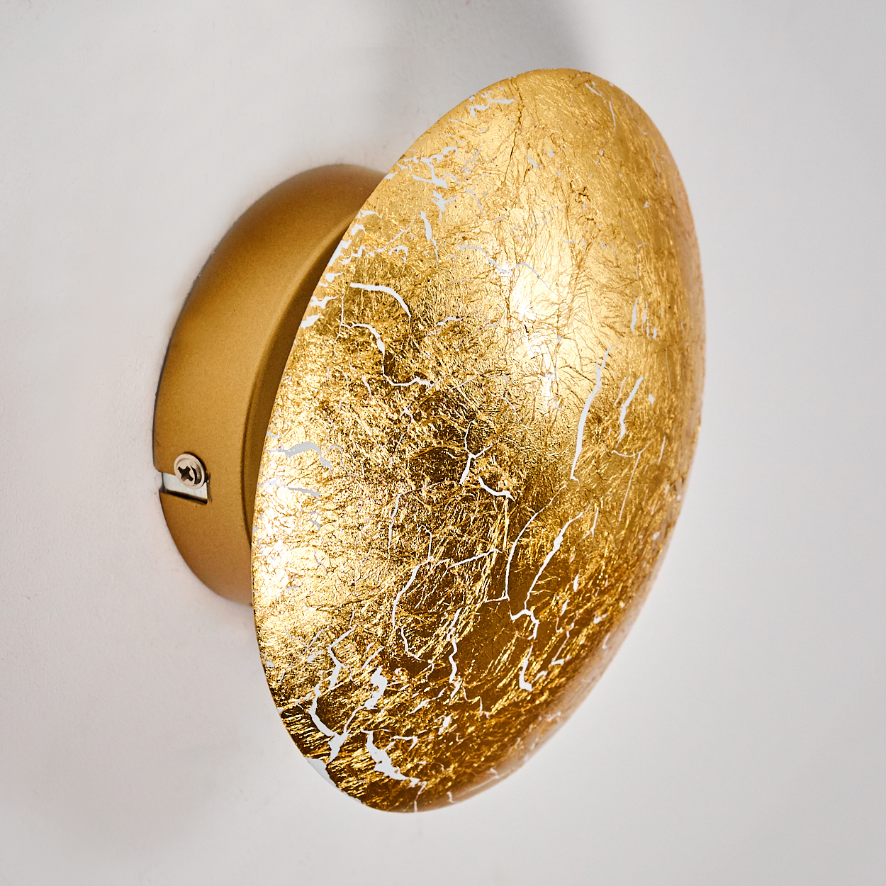 Eine Wandleuchte aus Blattgold ist an einer weißen Wand montiert. Die Lampe hat einen runden, goldfarbenen Schirm mit weißem Krakelierungseffekt.