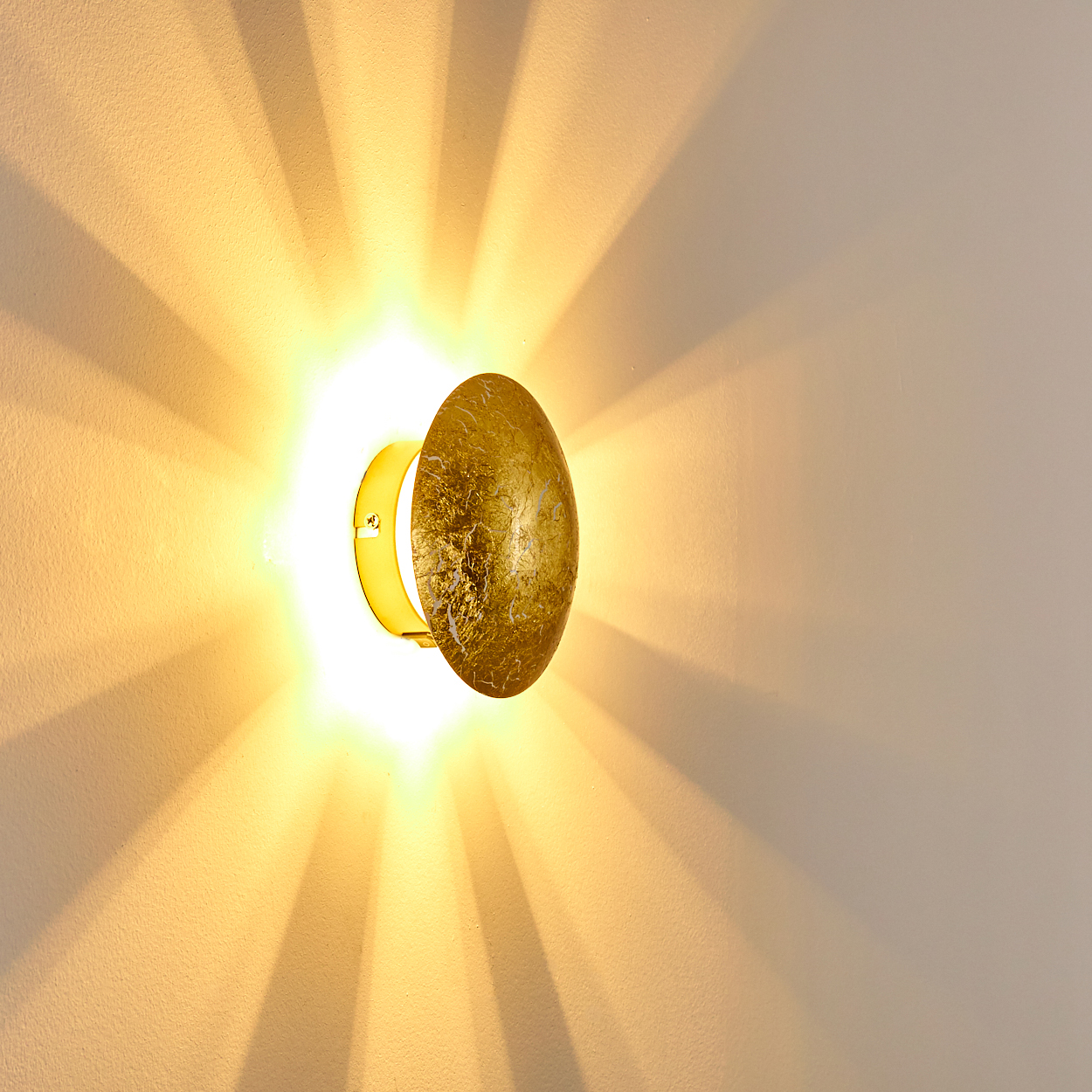 Eine goldene Wandleuchte mit ovalem Schirm und Ring. Licht strahlt von der Lampe auf die Wand.