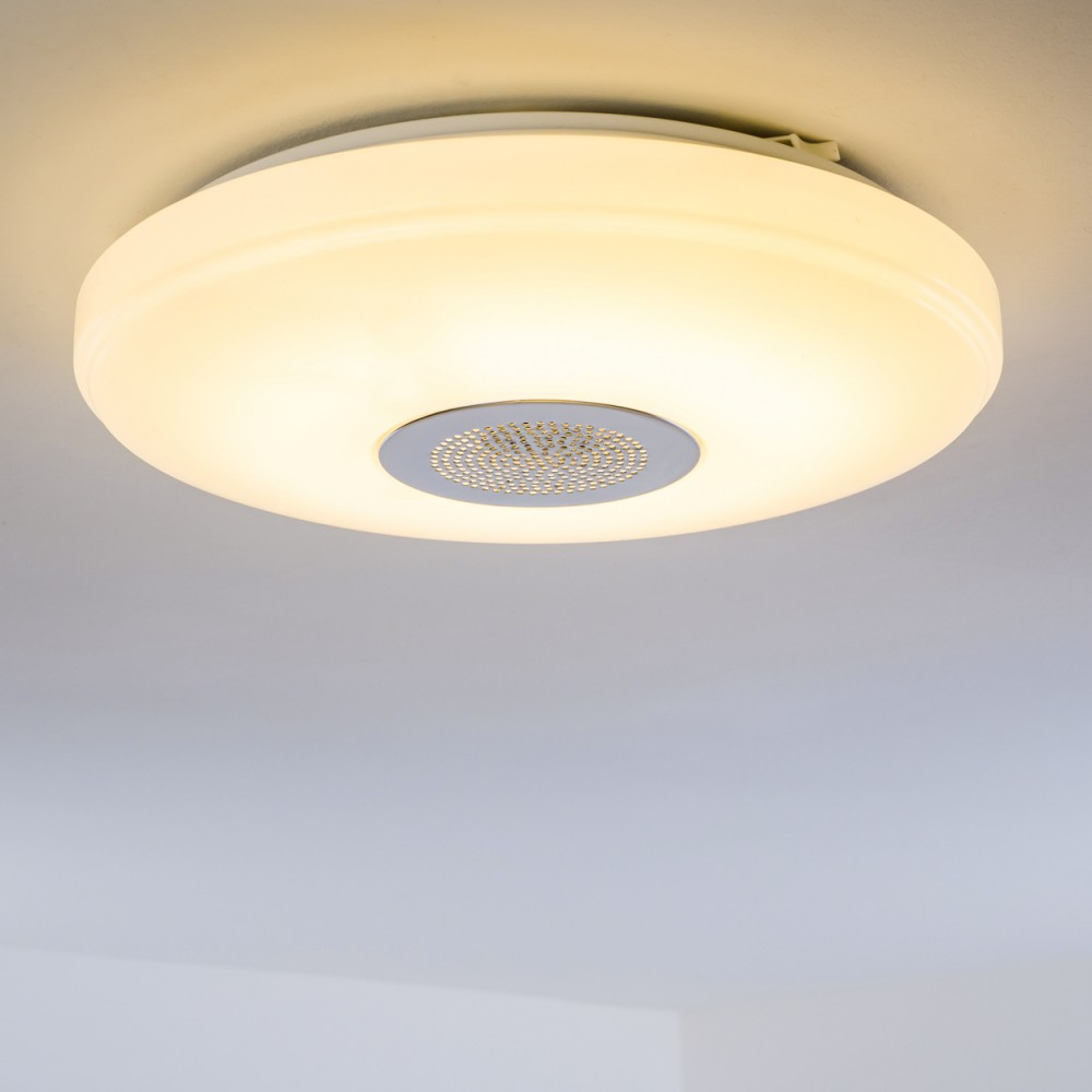 Eine runde, weiße Deckenleuchte mit einem zentralen, perforierten Metalllautsprecher. Das Licht strahlt warm gelb.
