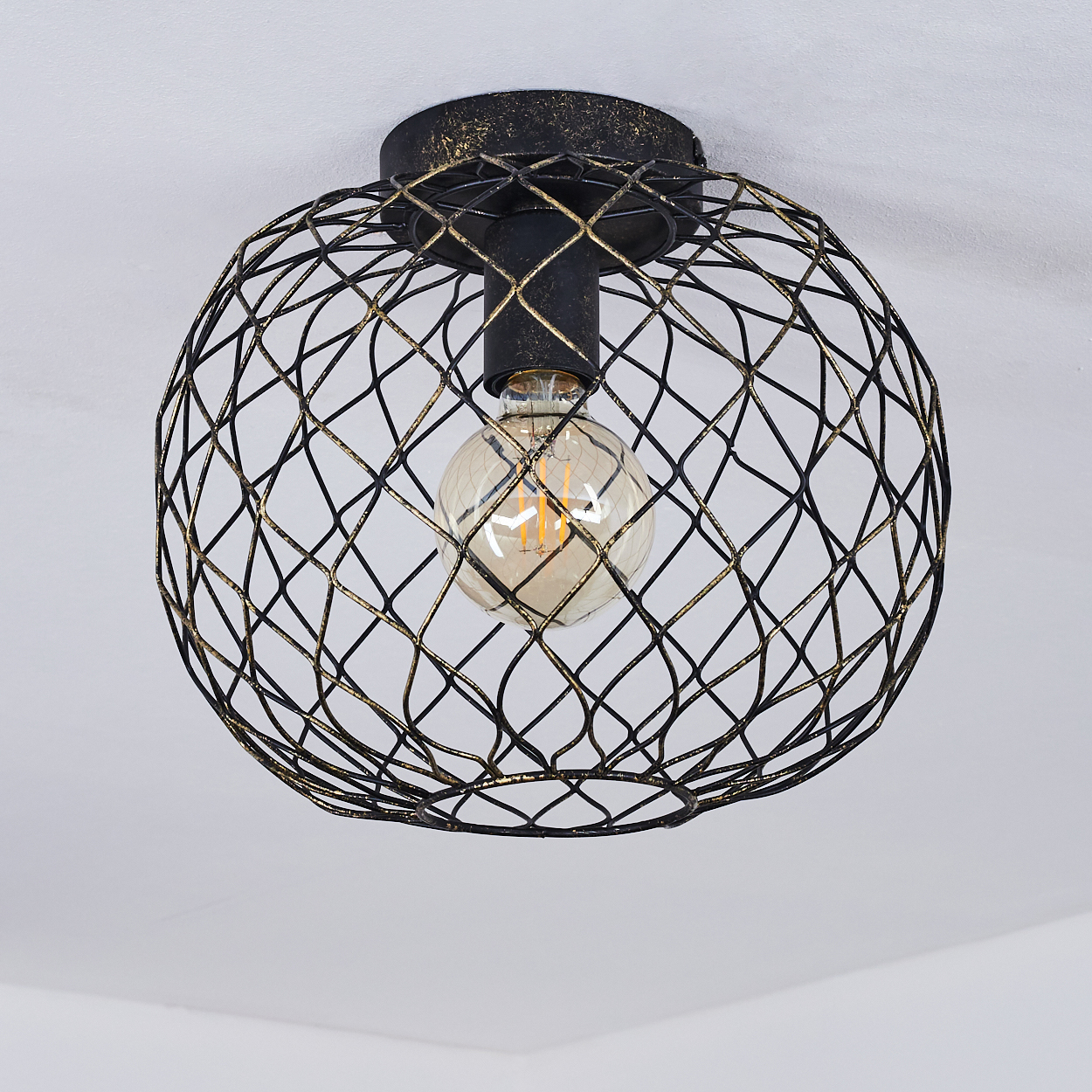 Eine schwarze Metallkäfig-Leuchte mit einer warmen Glühbirne im Inneren. Die Käfig ist an einer weißen Decke montiert.
