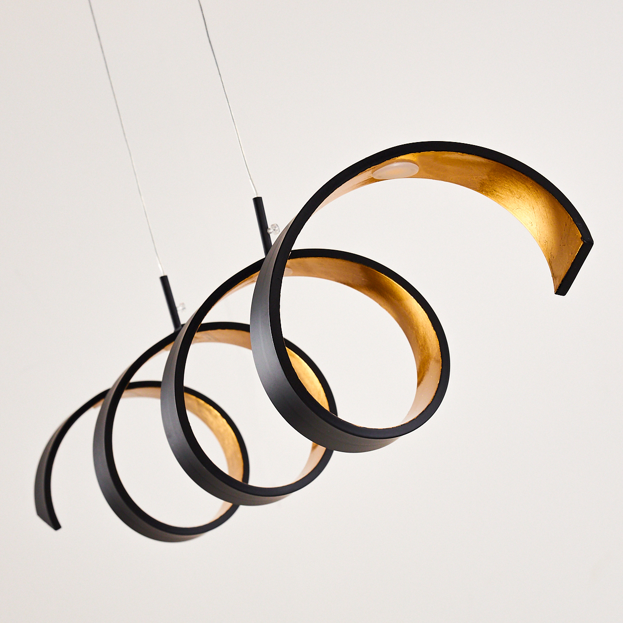 Moderne Hängelampe mit schwarzen, bandartigen Spiralen, goldener Innenseite, an dünnen Drähten vor weißem Hintergrund.