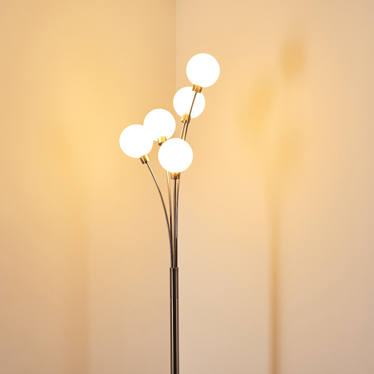Eine moderne Stehlampe mit fünf kugelförmigen weißen Glühbirnen. Die Lampe hat einen Metallstiel und steht in einer Ecke.