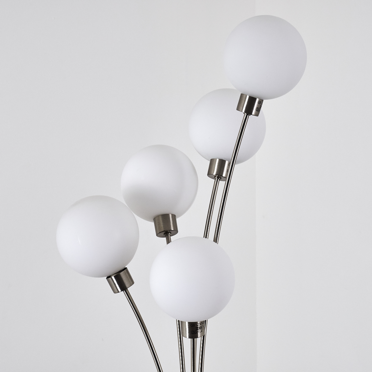 Eine moderne Lampe mit fünf weißen, kugelförmigen Glühbirnen an dünnen Metallstielen, vor weißem Hintergrund.