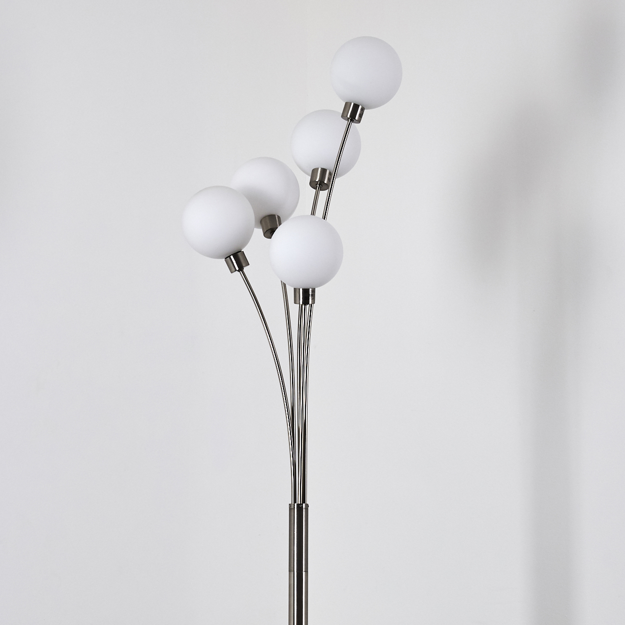 Eine Stehlampe mit fünf weißen Kugelleuchten, die sich von einem zentralen Metallmast erstrecken. Der Hintergrund ist eine helle Wand.