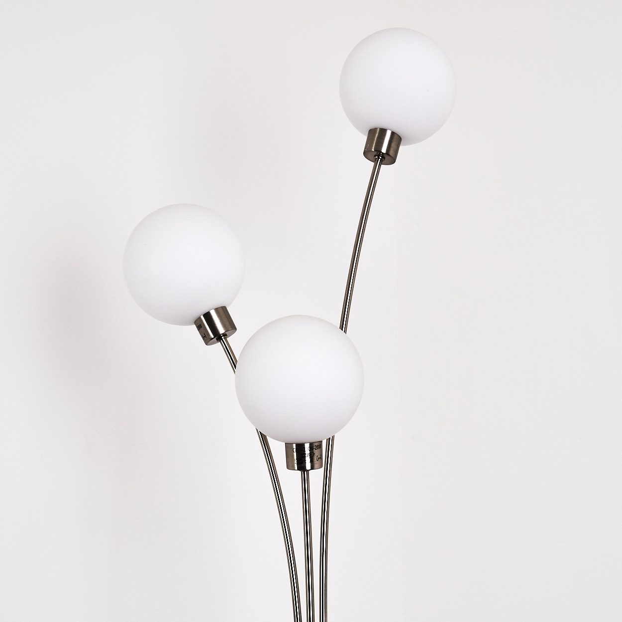 Eine moderne Lampe mit drei weißen, kugelförmigen Schirmen und silbernen Stielen vor weißem Hintergrund. Die Schirme sind gleichmäßig verteilt.