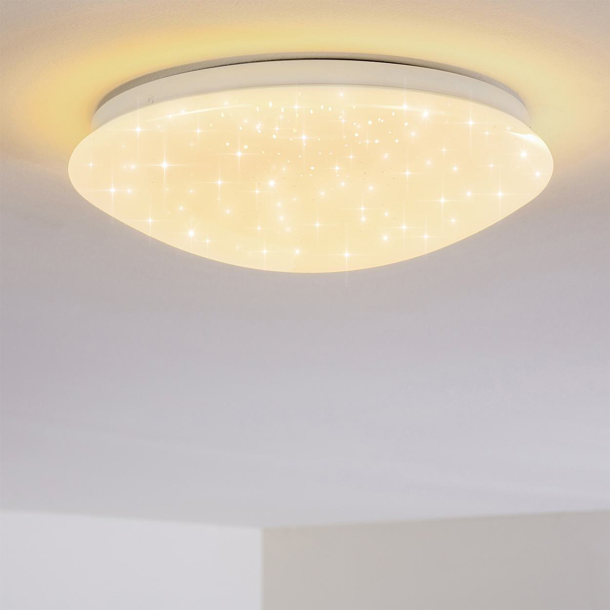 Eine Deckenleuchte mit sternförmigem Muster. Das Licht ist rund und weiß und erhellt die Decke mit einem sanften Schein.