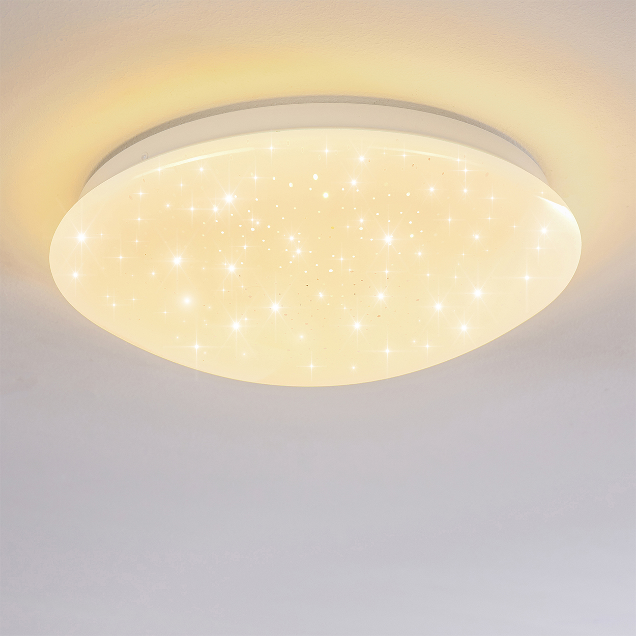 Eine weiße, ovale Deckenleuchte mit sternförmiger, beleuchteter Oberfläche. Der Hintergrund ist eine schlichte, hellfarbige Decke.