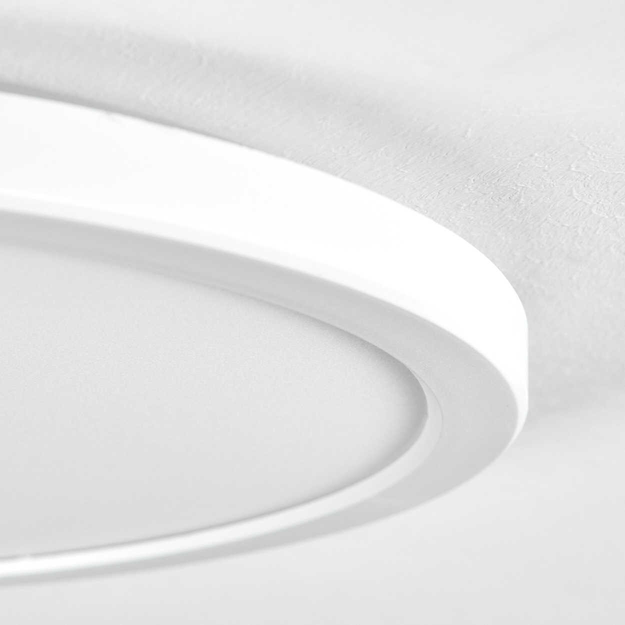 Nahaufnahme einer weißen, oval geformten Deckenleuchte, mit einer strukturierten weißen Decke im Hintergrund.