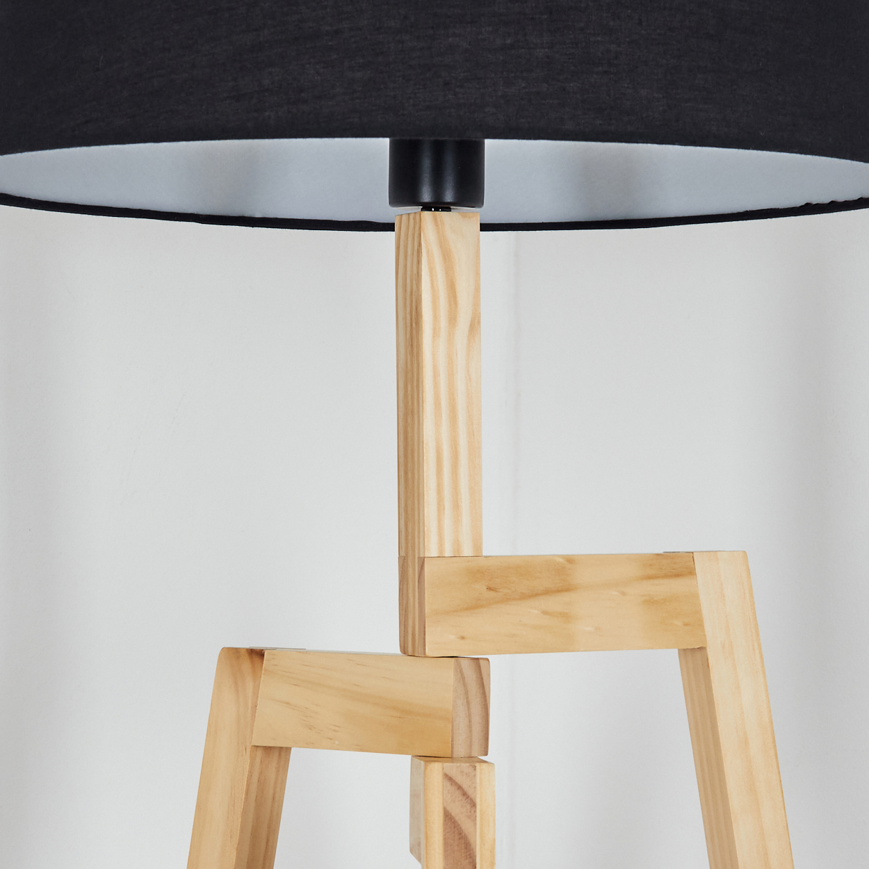 Eine Holzlampe mit schwarzem Lampenschirm. Die Lampe hat einen hellen Holzsockel und steht vor einer weißen Wand.