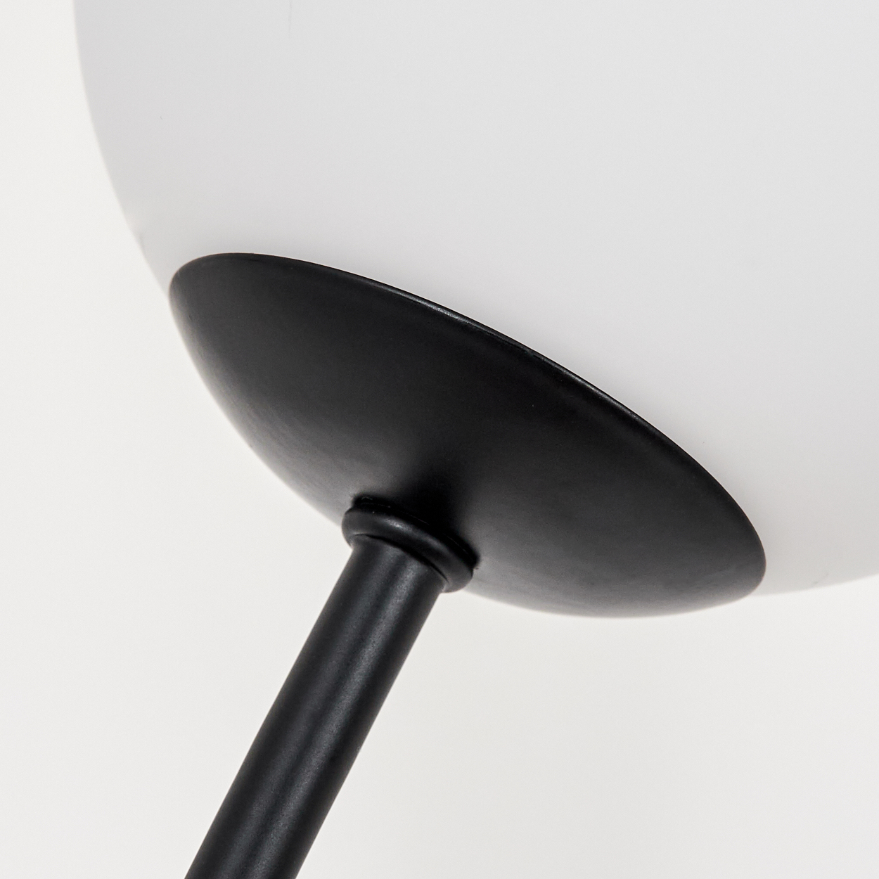 Nahaufnahme einer modernen Lampe. Ein weißer Lampenschirm befindet sich über einem schwarzen, kreisförmigen Sockel und einem schwarzen Stiel auf weißem Hintergrund.
