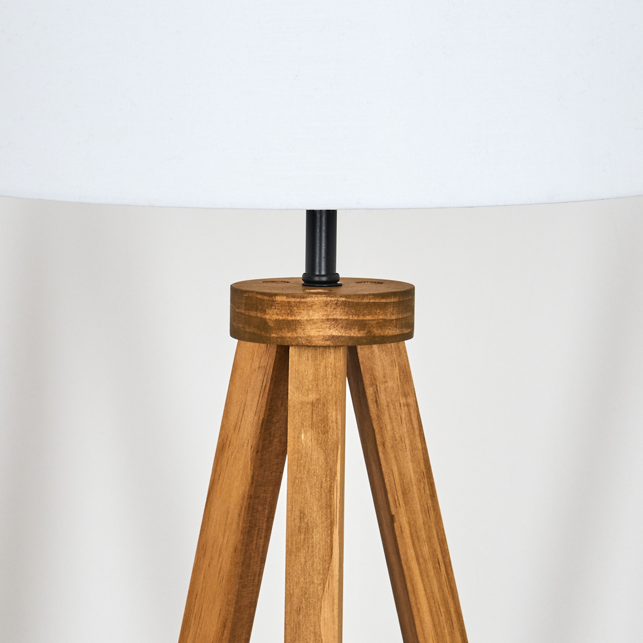 Ein hölzernes Stativ-Lampenfuß mit weißem Lampenschirm. Die Lampe hat eine schwarze Metallstange, die den Sockel und den Schirm verbindet.