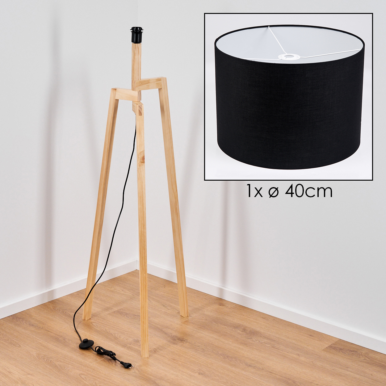 Eine hölzerne Stativ-Stehlampe mit schwarzem Lampenschirm. Ein schwarzes Netzkabel verläuft nach unten. Die Lampe steht in einer Ecke.