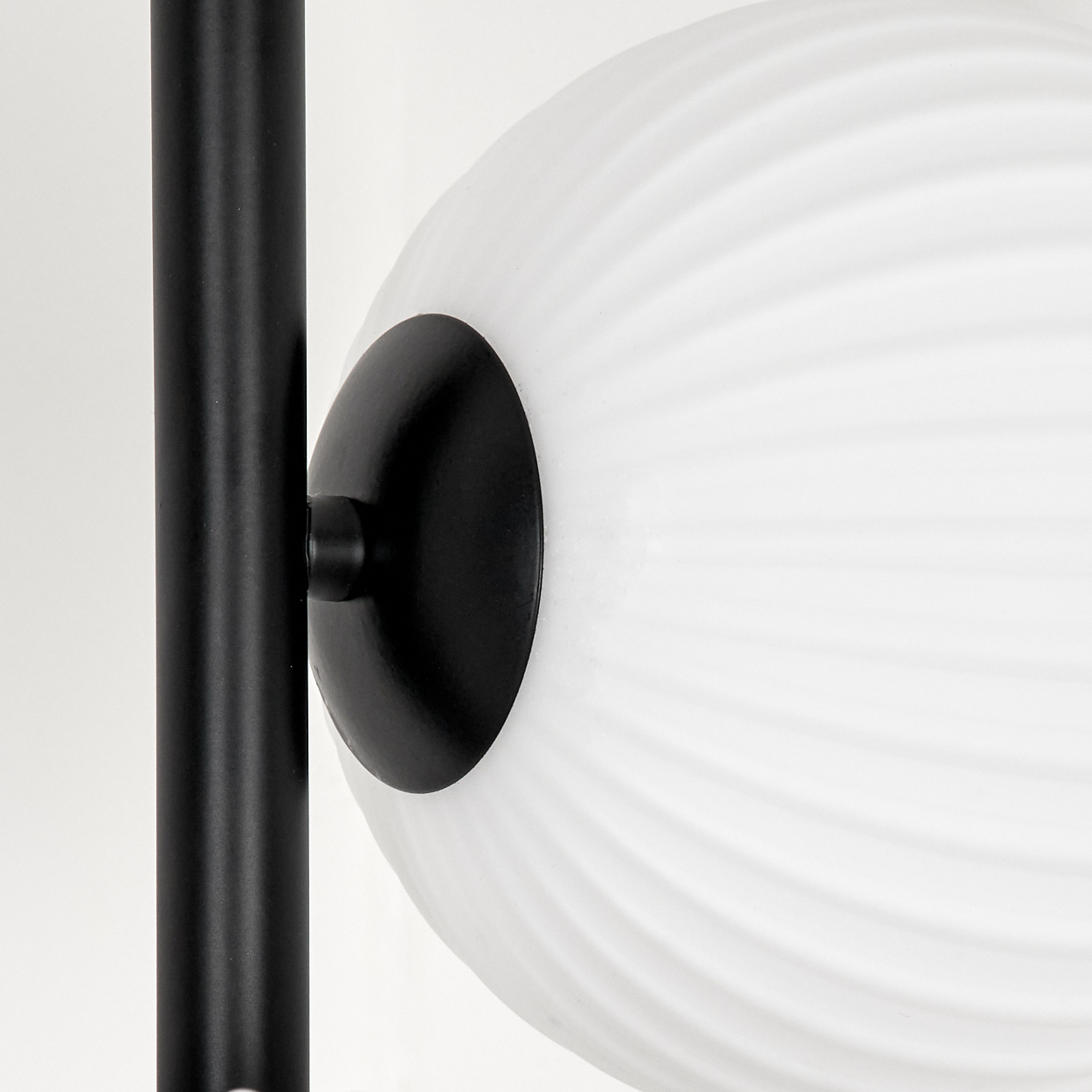 Nahaufnahme einer Lampe. Eine weiße, gerippte Glaskugel ist an einer schwarzen Metallstange befestigt. Der Hintergrund ist weiß.