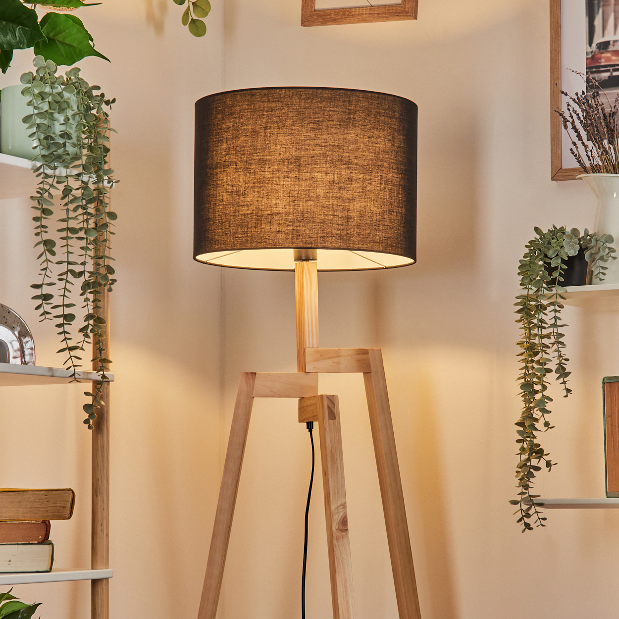 Eine Stehlampe aus Holz mit schwarzem Lampenschirm steht in einer Ecke. Regale mit Pflanzen und Büchern an den Wänden.