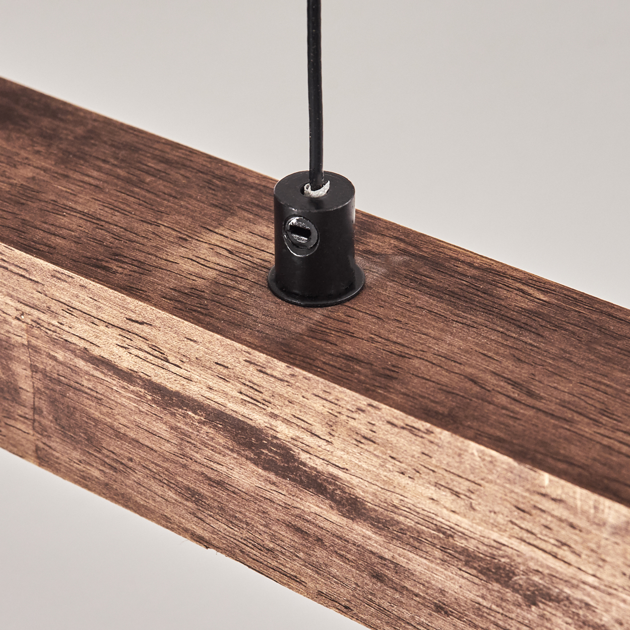Nahaufnahme eines Holzbalkens mit schwarzem Draht und Fitting. Das Holz ist braun, der Hintergrund ist weiß.