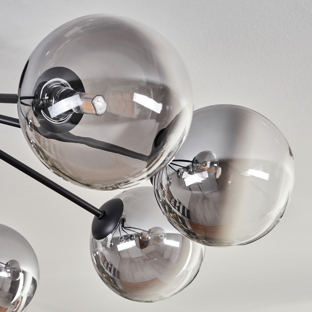 Nahaufnahme einer modernen Deckenleuchte mit mehreren kugelförmigen Glasschirmen, die Licht reflektieren. Schwarze Arme erstrecken sich von einem Mittelpunkt.