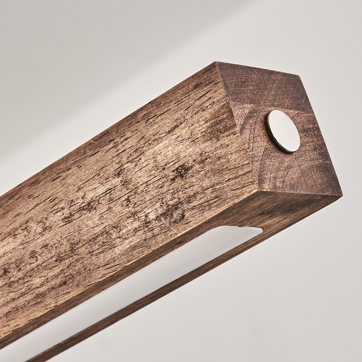Nahaufnahme eines Holzbalkens mit weißem Lichtstreifen und Metallscheibe. Der Hintergrund ist eine schlichte weiße Oberfläche.