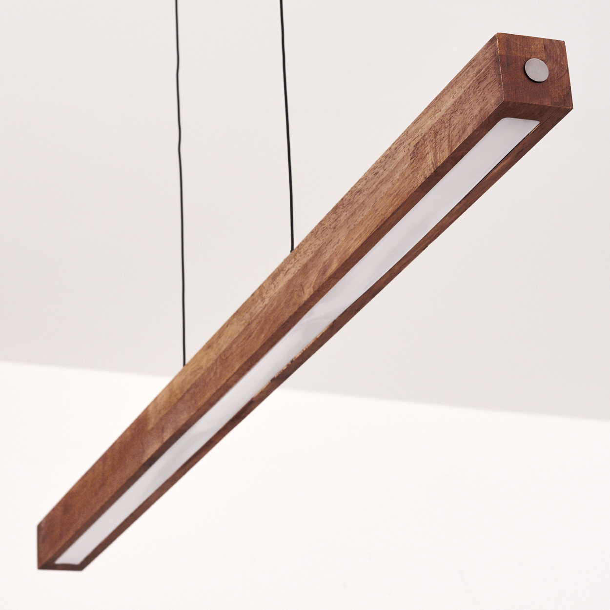 Eine rechteckige Holzlampen hängt an schwarzen Drähten. Die Lampe hat einen hellen weißen Lichtstreifen und einen Metallkreis.