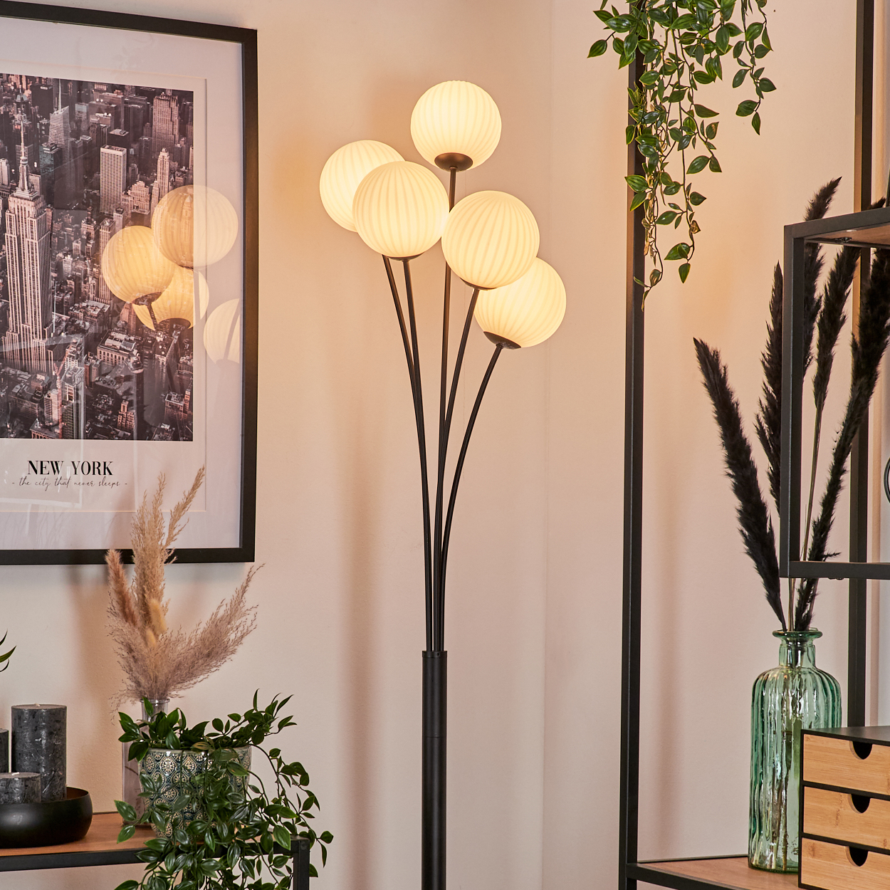 Ein Raum mit einer Stehlampe, einem gerahmten New York-Bild und dekorativen Pflanzen. Die Lampe hat mehrere Kugelleuchten.