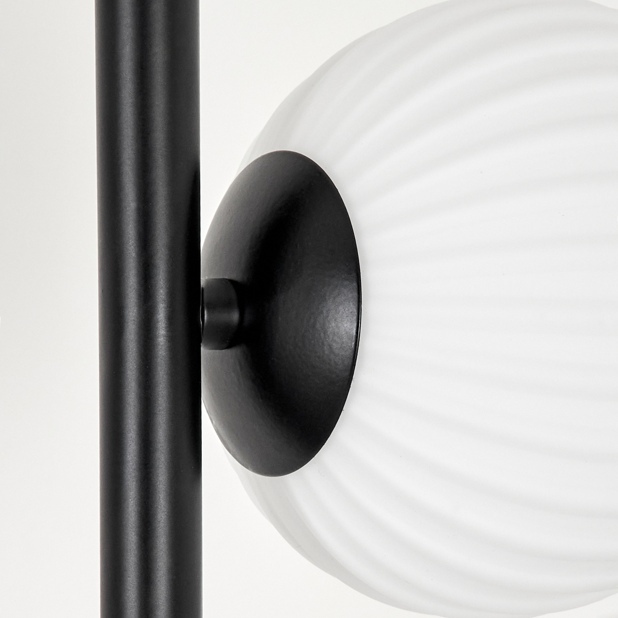 Eine schwarze Lampenstange mit einem großen, weißen, gerippten, kugelförmigen Lampenschirm. Der Lampenschirm ist über eine schwarze Scheibe an der Stange befestigt.