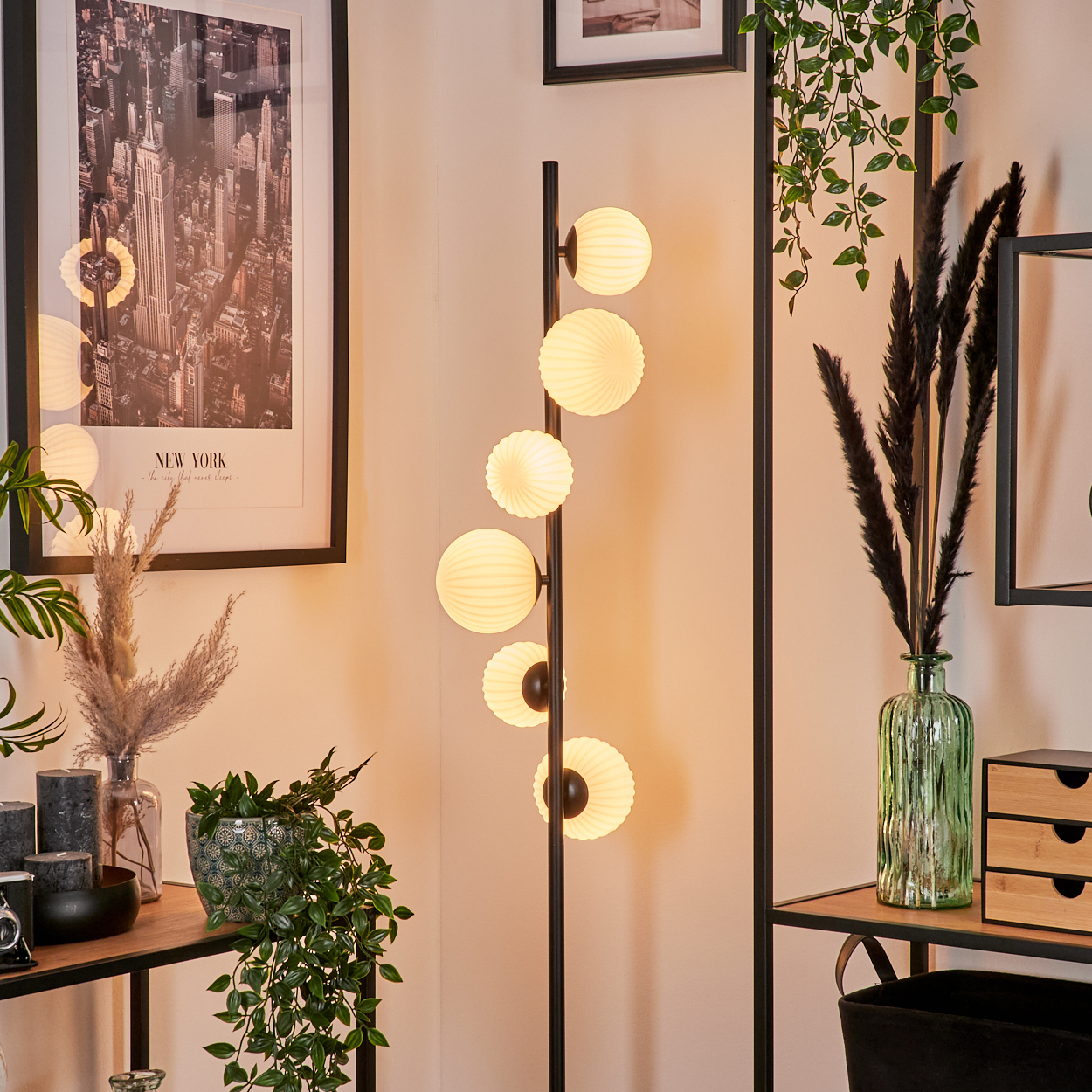 Ein modernes Raumarrangement mit Stehlampe, Kunst, Pflanzen und Regalen. Ein schwarzer Rahmen und New York-Kunst. Pflanzen im Vordergrund.