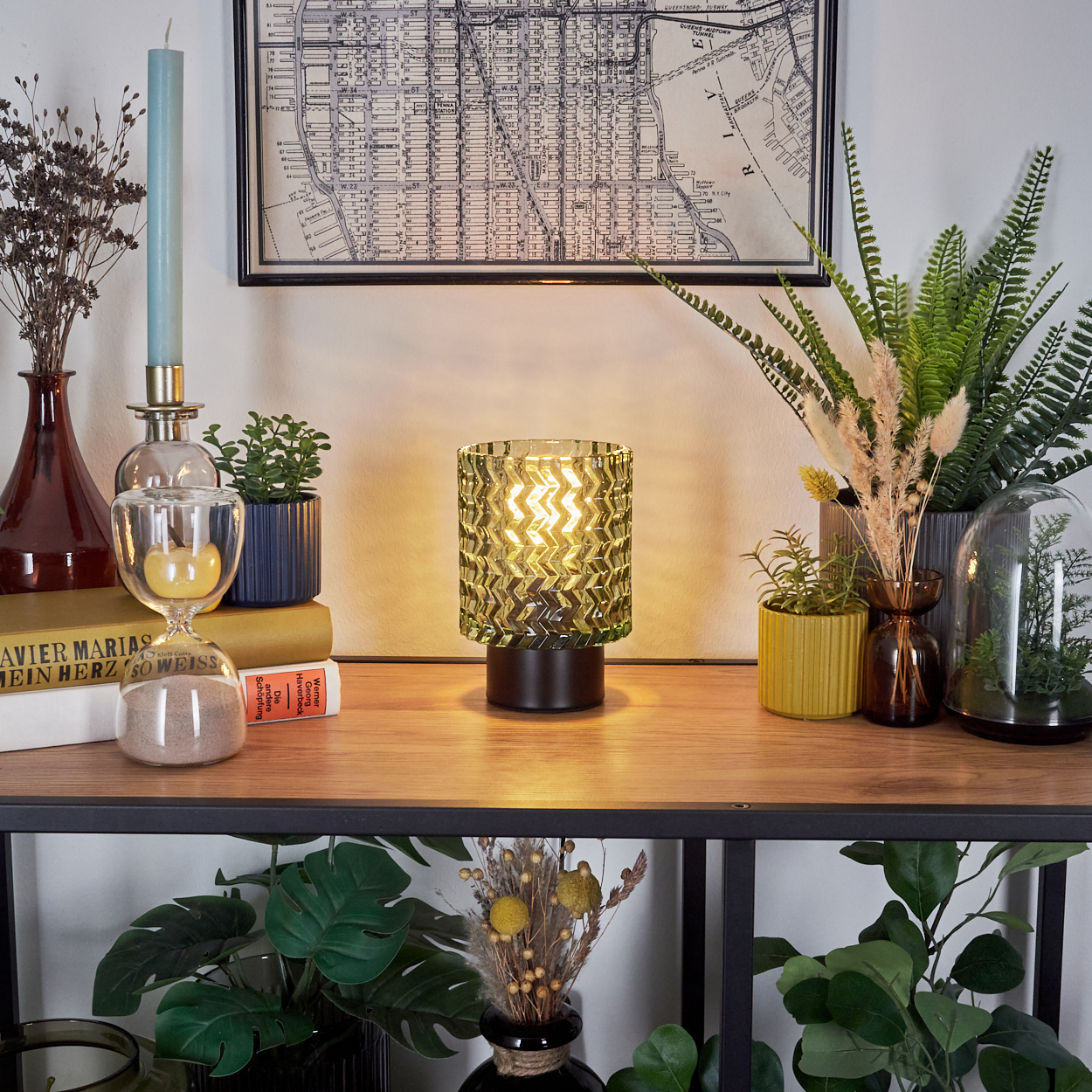 Ein Holzregal zeigt Dekor: eine Lampe, Pflanzen, Bücher, eine Karte, eine Kerze und Vasen. Der Hintergrund ist eine weiße Wand.