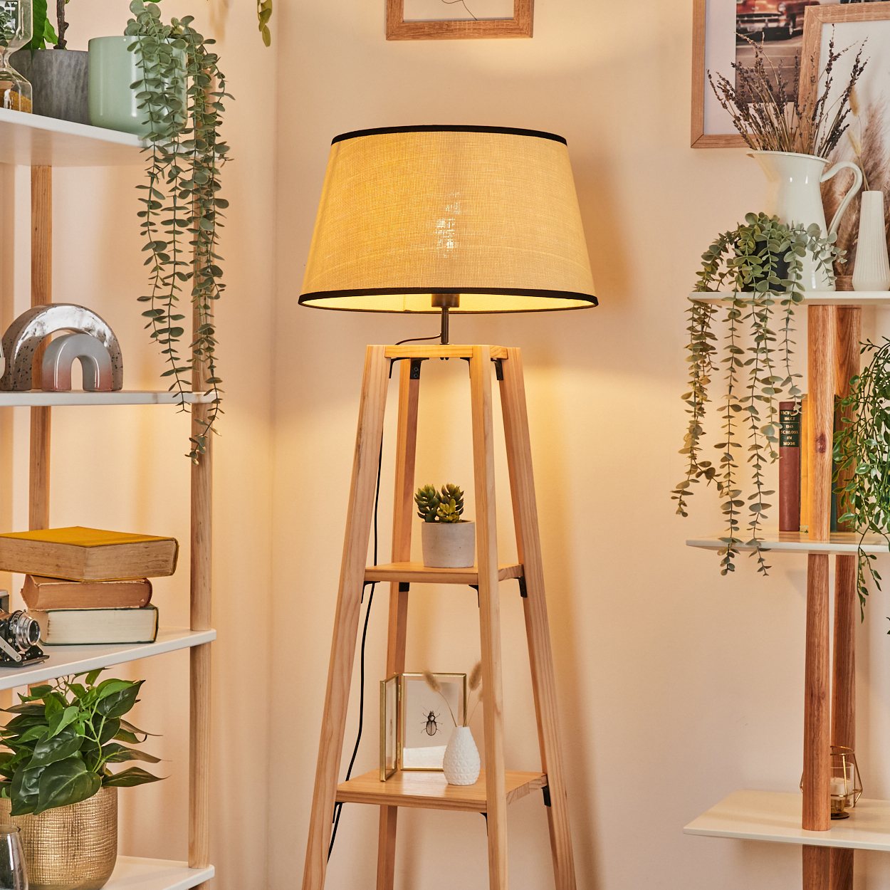 Eine Stehlampe aus Holz mit beigem Lampenschirm steht in einem Raum. Regale mit Pflanzen und Dekorationen befinden sich auf beiden Seiten. Sanfte Beleuchtung.