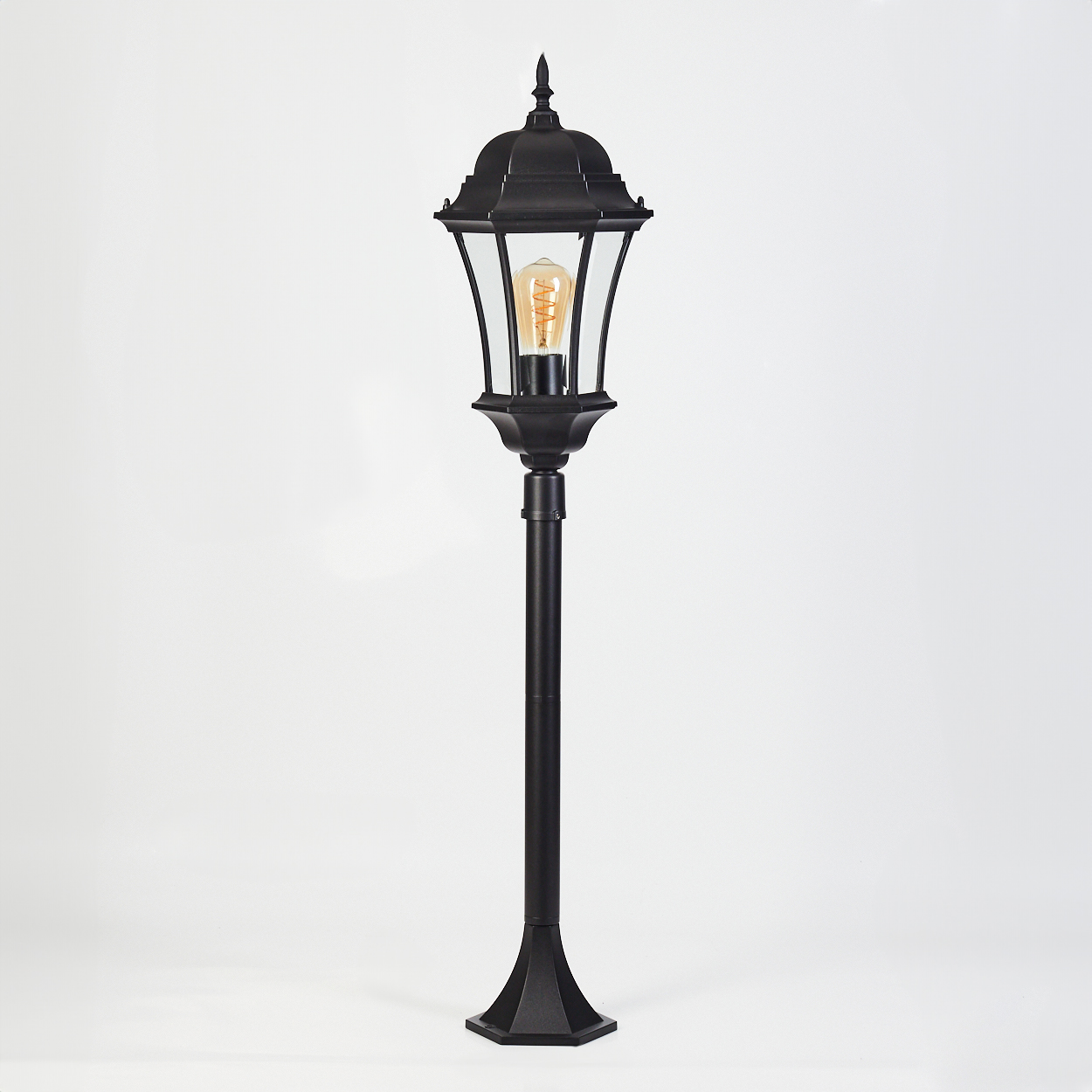 Eine schwarze Außenlampe vor weißem Hintergrund. Die Lampe hat eine dekorative Spitze, Glasscheiben und eine sichtbare Glühbirne.